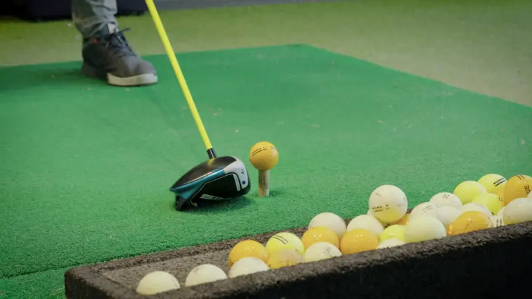 Driver in Ansprechposition hinter einem aufgeteeten Golfball, daneben ein Korb mit Übungsbällen