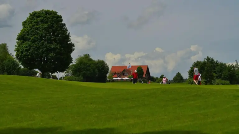 Golfplatz mit Golfern und Fahne auf dem Grün, im Hintergrund das Clubhaus