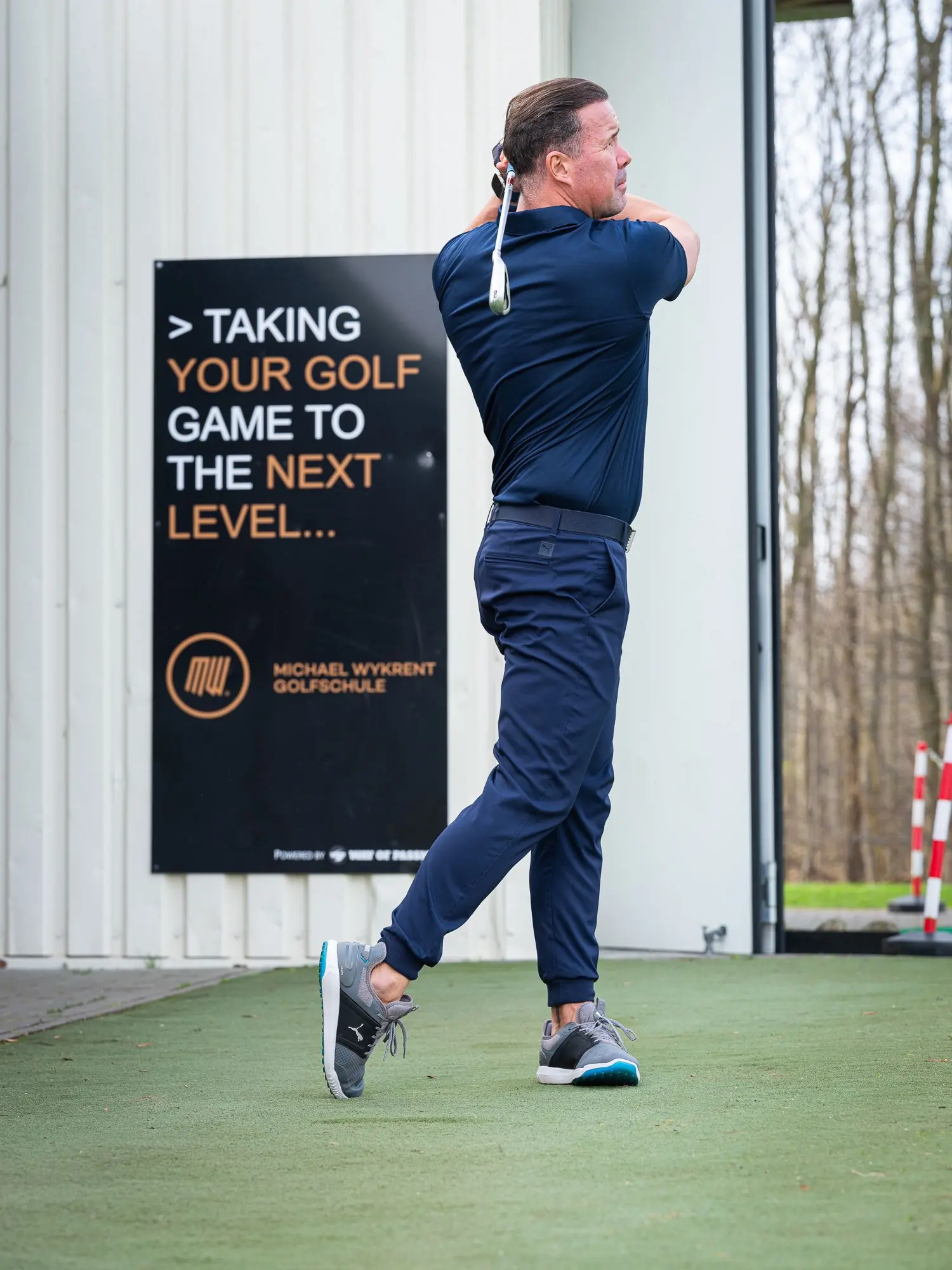 Michael Wykrent im Durchschwung vor dem Schild der Michael Wykrent Golfschule